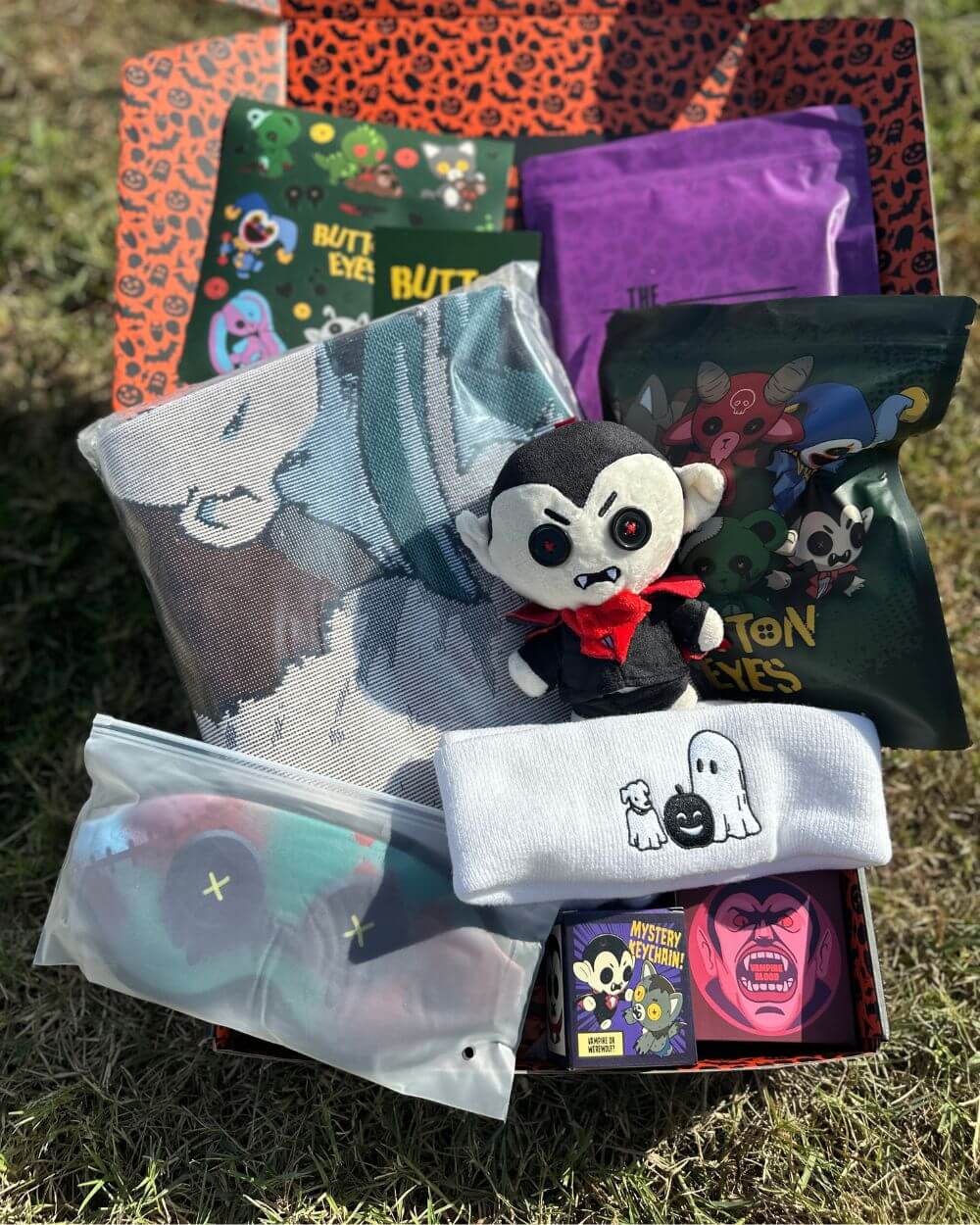 Collection of Halloween-themed items including a plush bat, small figurine, and various packaging on grass.