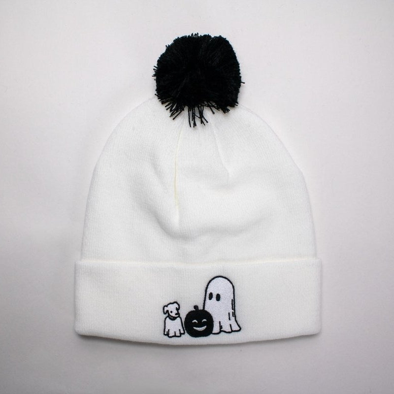 White beanie with black pom-pom and Halloween-themed ghost & ghost dog embroidery on a light gray background