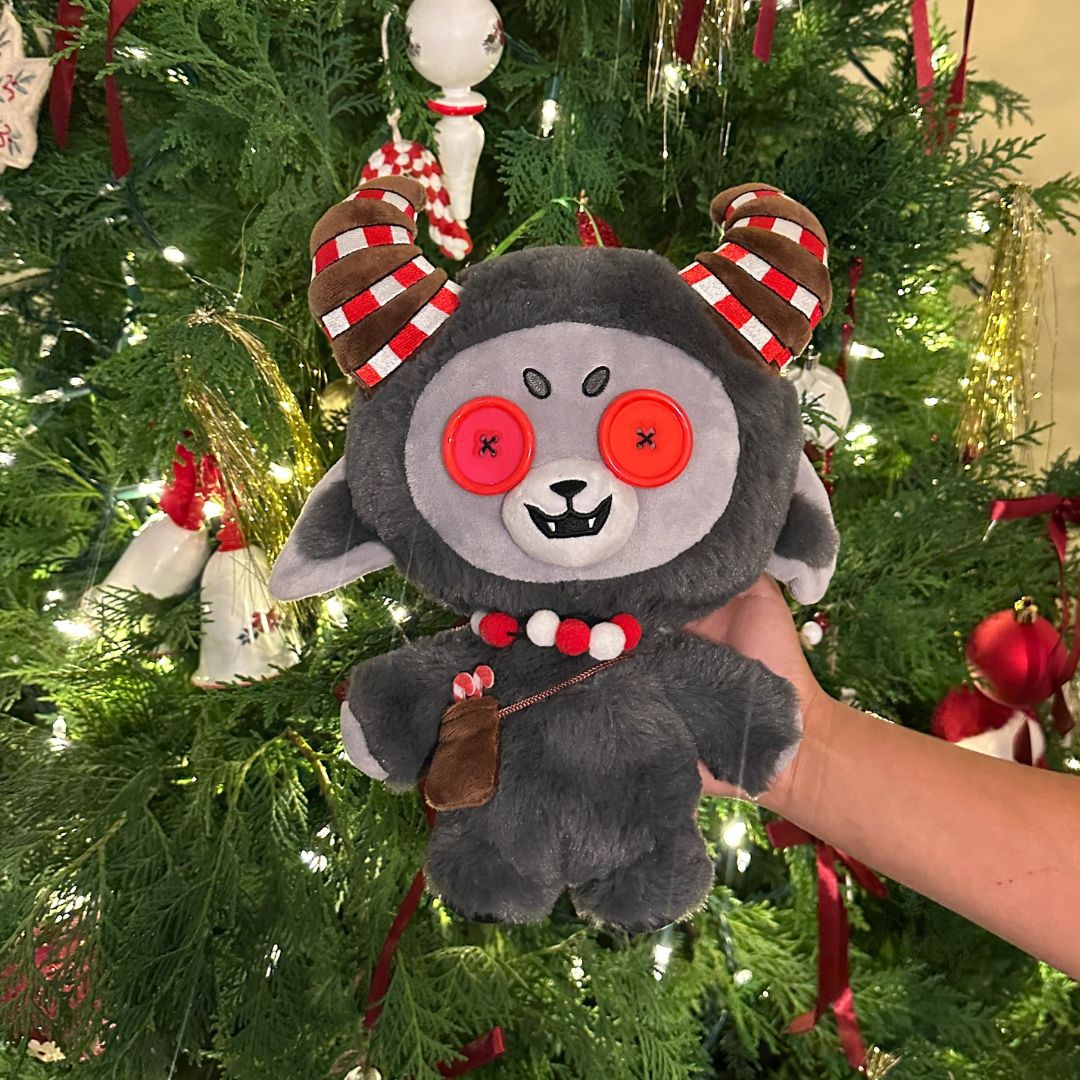 Kramplin the Goat plushie held in front of a Christmas tree