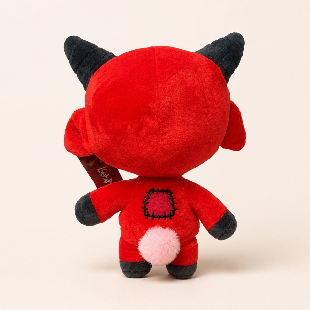 Red plush toy with black horns and pink heart on a beige background