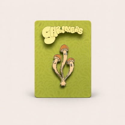 Enamel pin of mushrooms on a green card with 'Shroomers' branding.