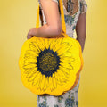 a large yellow flower shaped tote bag with a sunflower design printed on it in black with a girl in a dress wearing it