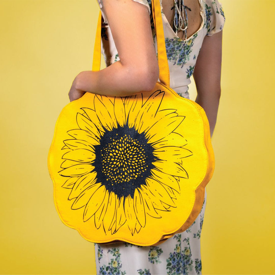 a large yellow flower shaped tote bag with a sunflower design printed on it in black with a girl in a dress wearing it