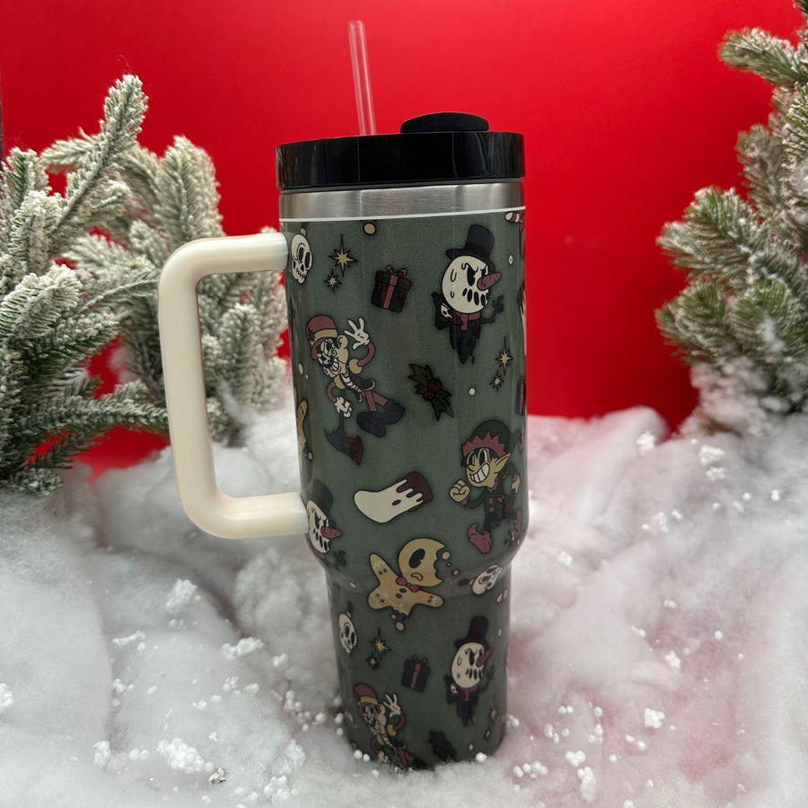 40oz Creepmas Tumbler. Double-walled, stainless stee, cream handle, green design on cup, standing on snow in red background