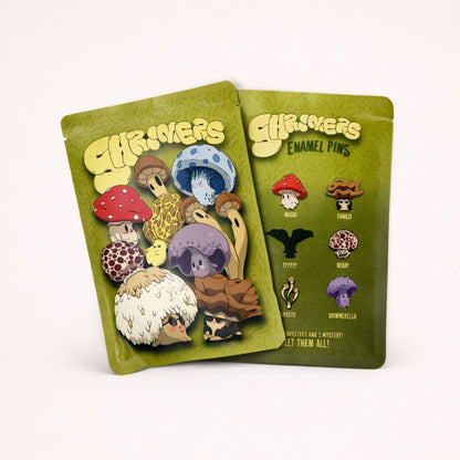 Two green packages of mushroom-themed enamel pins on a white background